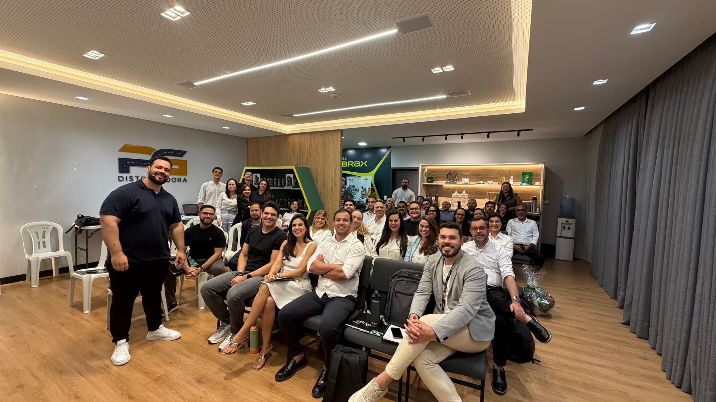 Turma reunida na sala de uma empresa durante um workshop presencial, com o instrutor em pé diante do grupo